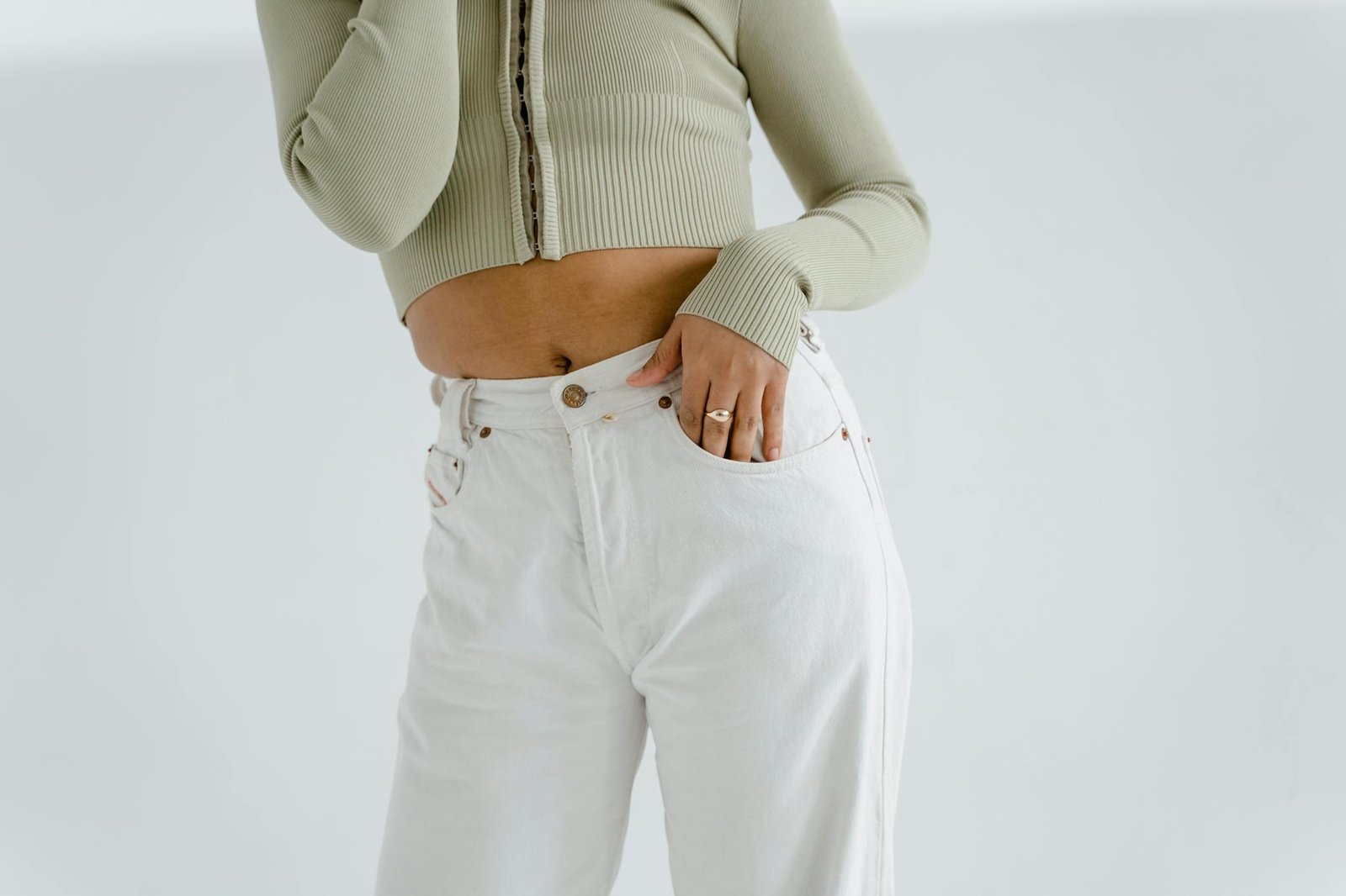 Minimalist fashion shot featuring a green sweater and white pants accessorized with rings.